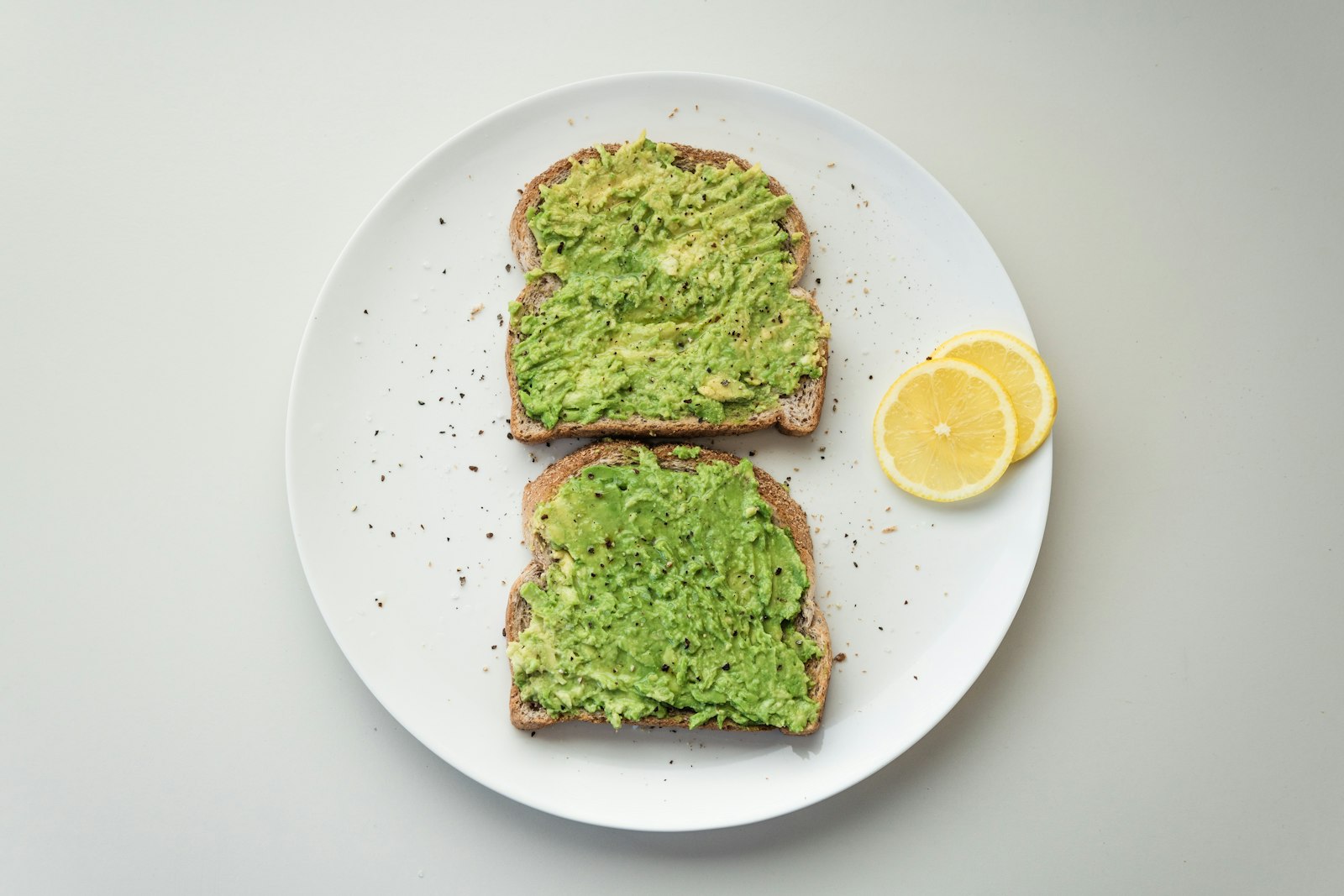 Slice of sourdough toast topped with smashed avocado, chilli flakes and lemon