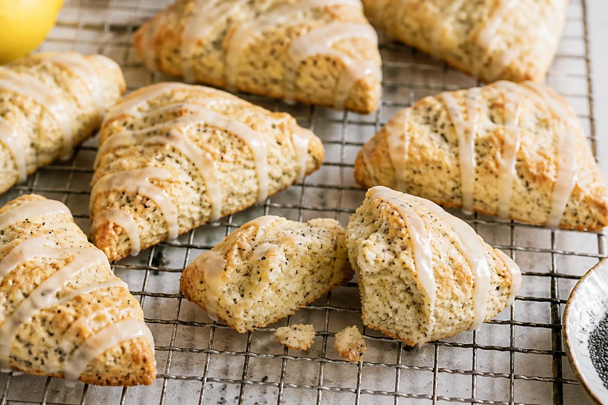 Triangular lemon poppy seed scones on a wire rack drizzled with white lemon glaze, one broken open to show the crumb