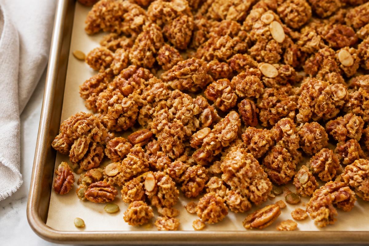 Sheet pan of crunchy golden maple pecan granola clusters with pecans, sliced almonds and pumpkin seeds