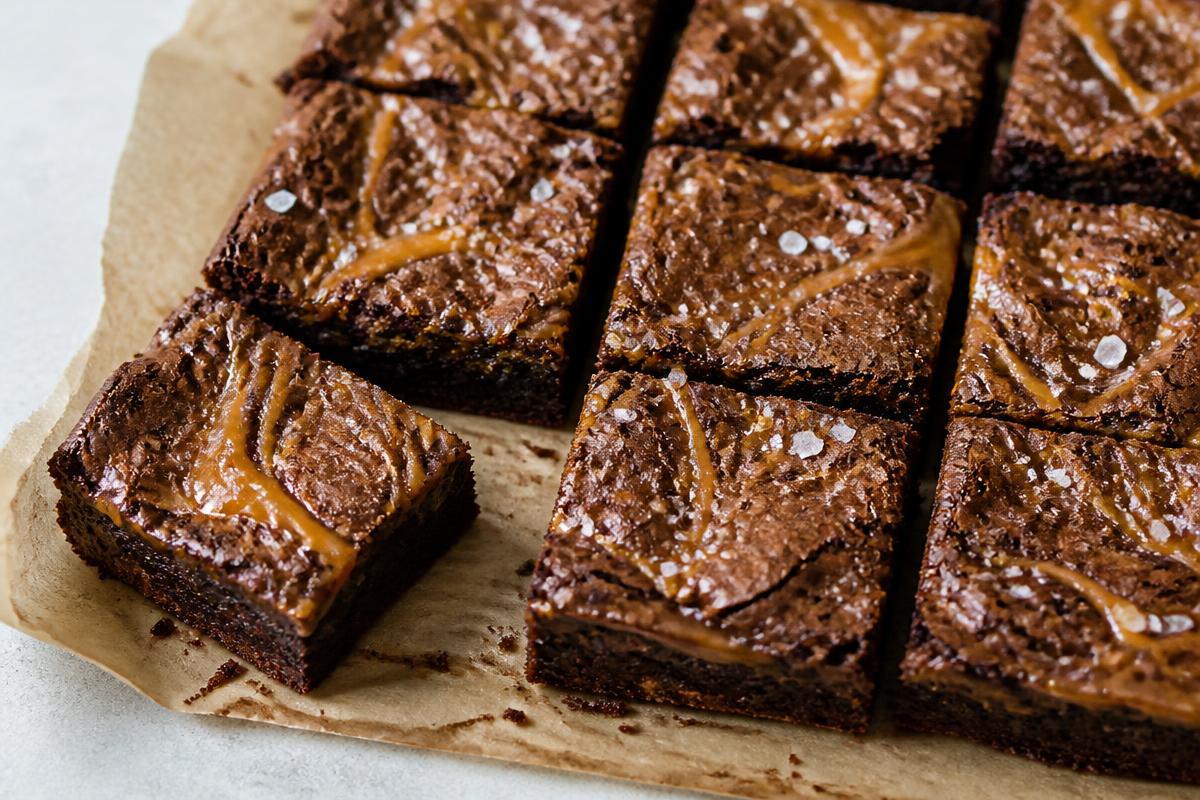 Salted caramel brownies cut into squares on parchment, with a fudgy dark crumb, caramel swirls and flakes of sea salt.